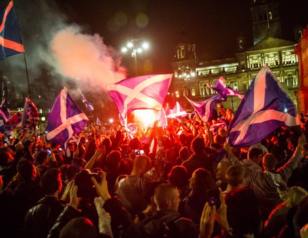 A crowd with Scotland flags at night in George Square Glasgow